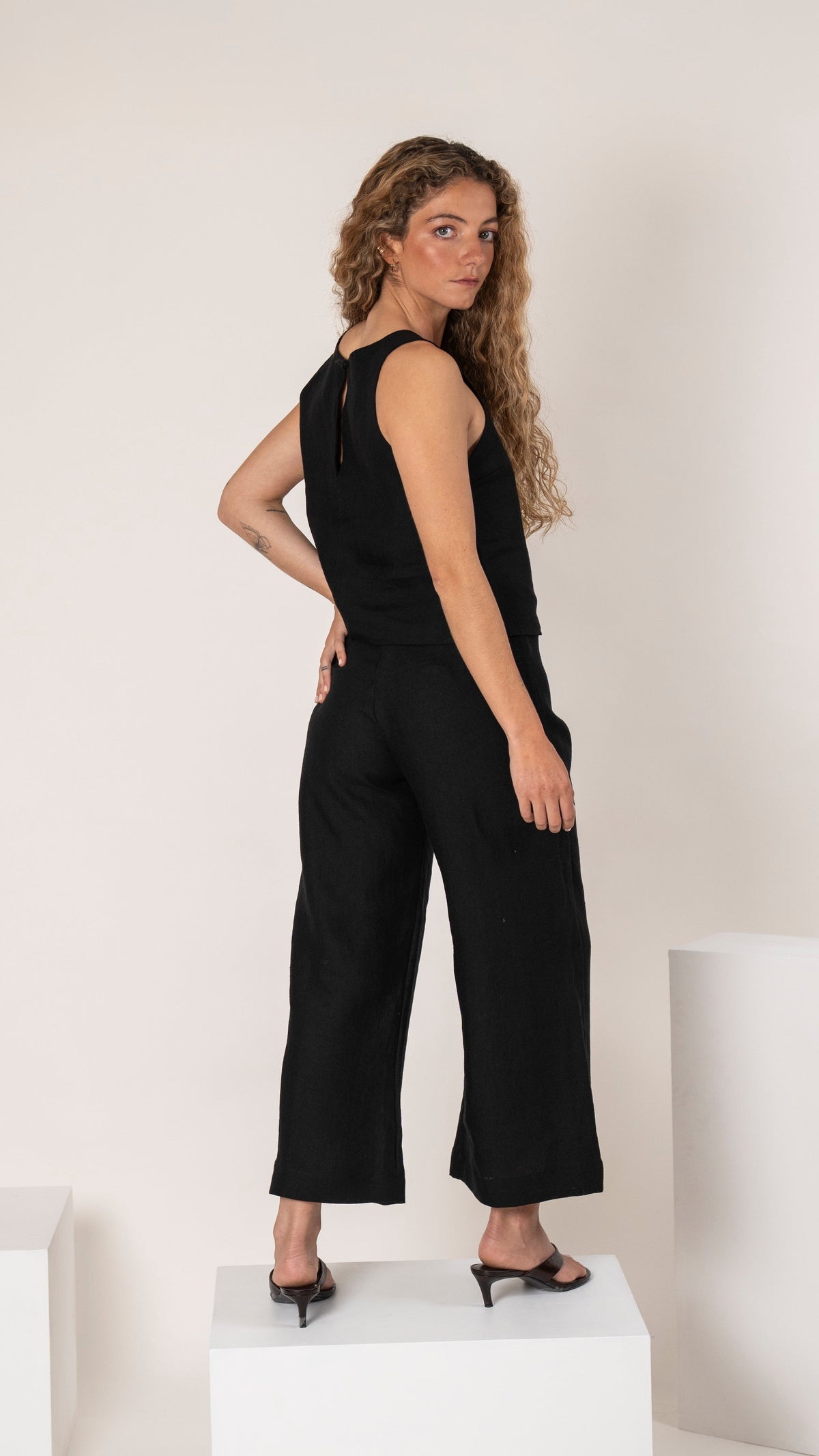 Top de lino negro con botón, sin mangas y ajustado, con pantalón de lino negro con pinzas, de frente