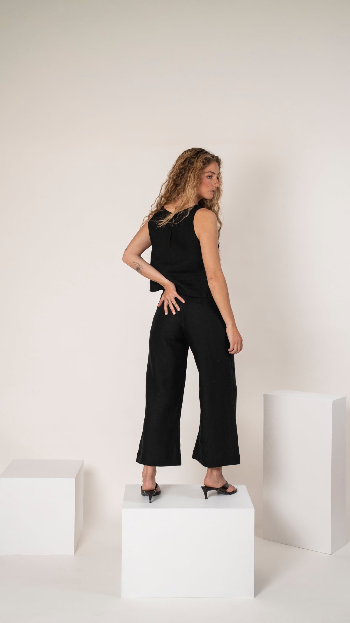 Pantalón de lino negro con pinzas y top negro sin mangas, vista de perfil